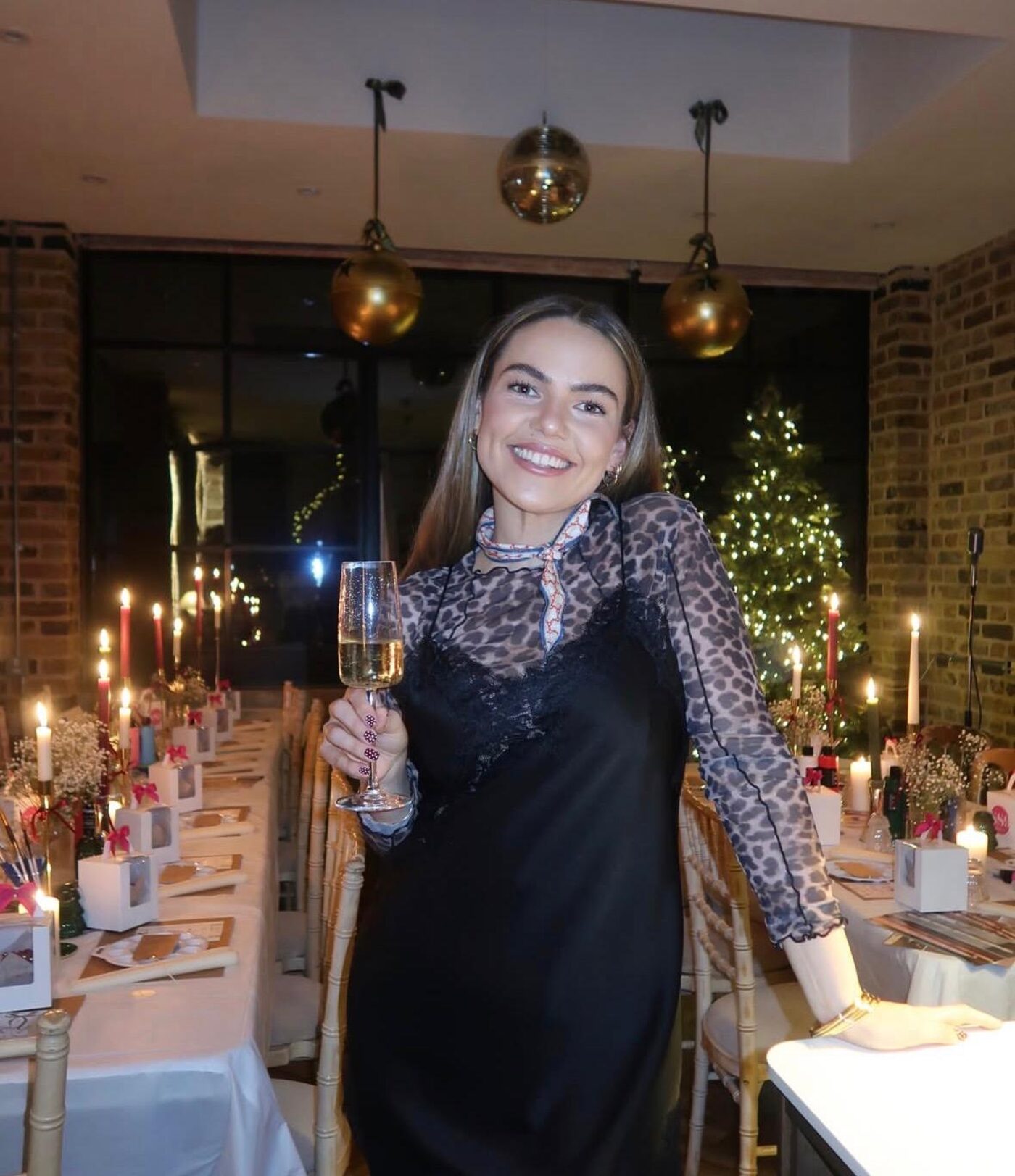 Host raising a glass of fizz in front of candlelit tables and a Christmas tree