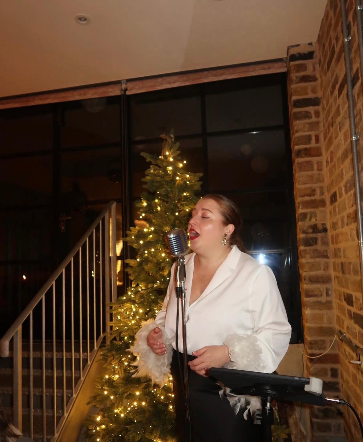 Live singer performing beside a lit Christmas tree