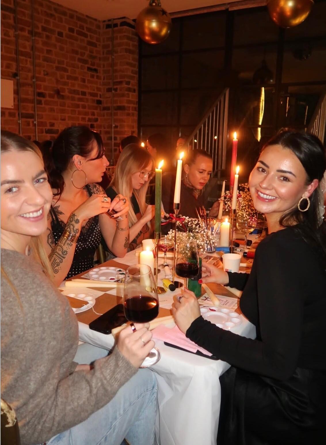 Guests smiling around a candlelit table at a candle painting workshop